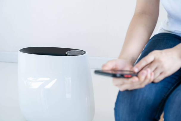 Woman using smartphone to control the modern air purifier, a smart home and automation technology devices concept. Healthcare and wellbeing accessory in lifestyle. Woman control air purifier from app. - Foto, immagini