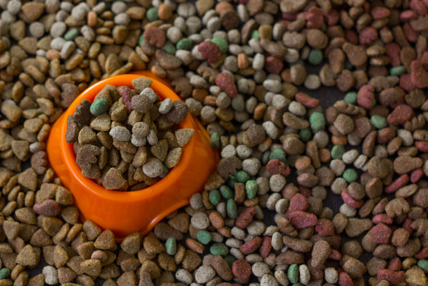 Cuenco de plástico naranja lleno de comida seca para mascotas rodeado de comida seca para gatos y perros - Foto, imagen