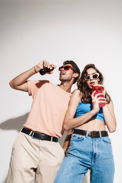 Image of funny beautiful couple dancing while drinking beverages isolated over white background - 写真・画像