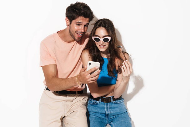 Image of attractive excited couple expressing surprise while using cellphone isolated over white background - Valokuva, kuva