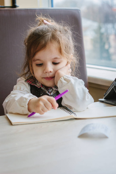 Маленька дівчинка, яка пише або малює ручкою в книзі
. - Фото, зображення