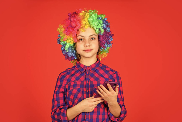 small girl colorful wig use smartphone. positive and cheerful. childhood happiness. kid looking funny in rainbow wig hair. hair dyeing at hairdresser. child having fun. happy birthday party - Photo, image