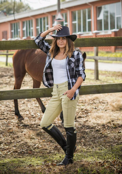 Amerikkalainen nainen hevostilalla. Muotokuva tytöstä cowboy-hatussa hevosineen. Hippoterapia luonteeltaan - Valokuva, kuva