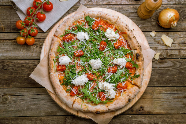 delicious Italian pizza with arugula leaves, tomatoes and cheese  on wooden table - Foto, immagini