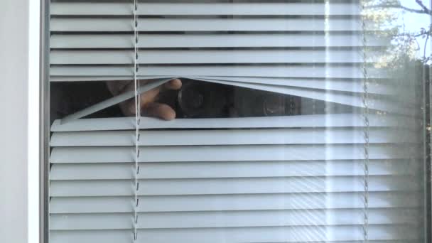 Мужчина наблюдает с биноклем через жалюзи в окне. - Кадры, видео