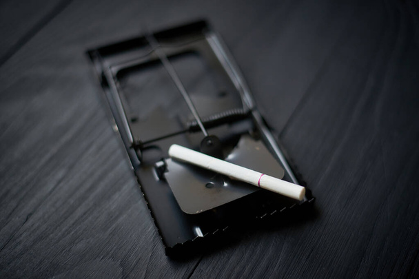 Сигарета в мышеловке на черном фоне. - Фото, изображение