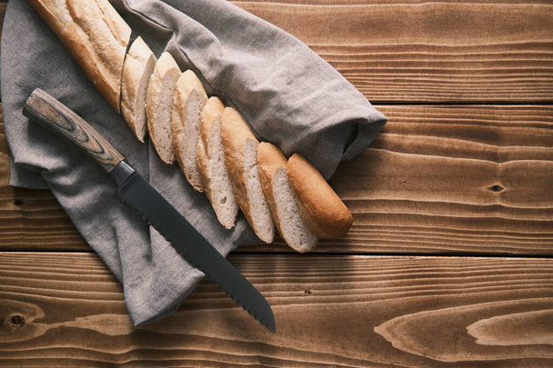 Top view fresh sliced French baguette on a linen cloth with knife on a wooden table - Fotografie, Obrázek