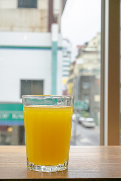 A glass of fresh orange juice drink on brown table with downtown window view background. - Photo, Image