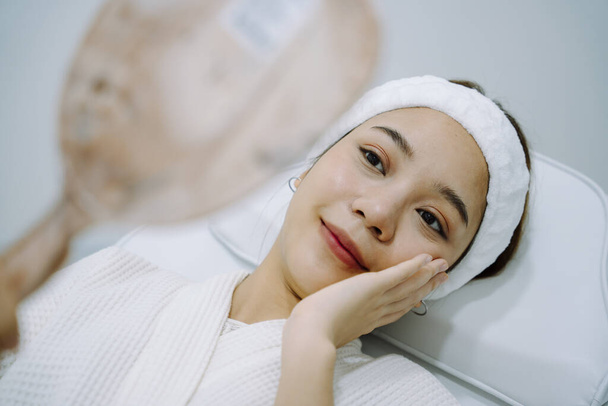Ázsiai nő néz tükör befejezése után spa kezelés kozmetikai klinikán. - Fotó, kép