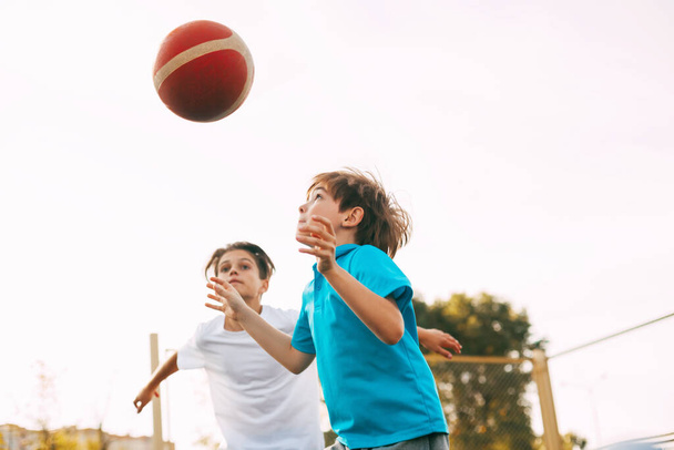 Két tini fiú kosarazik a játszótéren. A sportolók a labdáért harcolnak a játékban. Egészséges életmód, sport, motiváció - Fotó, kép