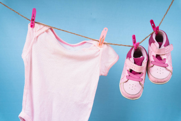 Детская рубашка и обувь висят на вешалке после стирки на синем фоне. - Фото, изображение