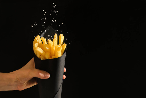 French fries in black paper cone and salt - Foto, Bild