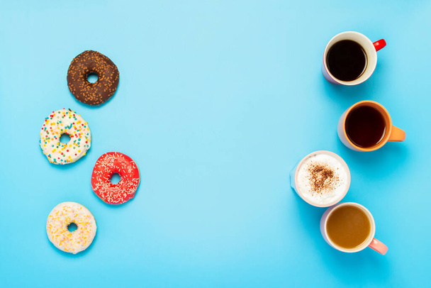 Lekkere donuts en kopjes met warme dranken op een blauwe achtergrond. Concept van snoep, bakkerij, gebak, coffeeshop, vrienden, vriendelijk team. Vlakke lay, bovenaanzicht. - Foto, afbeelding