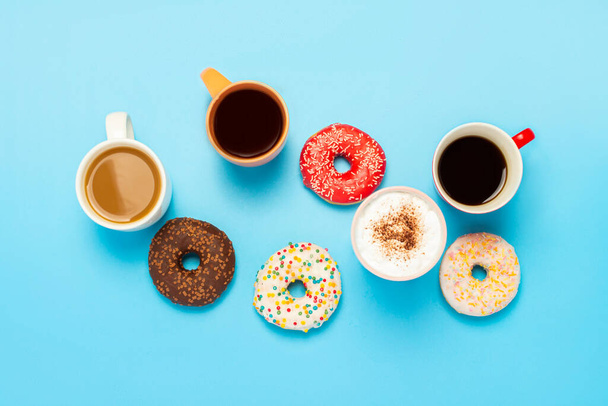 Lekkere donuts en kopjes met warme dranken, koffie, cappuccino, thee op een blauwe achtergrond. Concept van snoep, bakkerij, gebak, coffeeshop, vergadering, vrienden, vriendelijk team. Vlakke lay, bovenaanzicht. - Foto, afbeelding