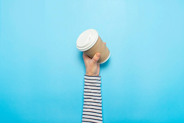Female hand holds a paper cup with coffee on a blue background. Concept of coffee, a warming drink, breakfast. Banner Flat lay, top view. - Foto, Imagem