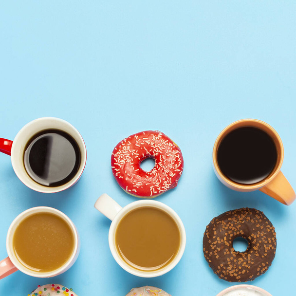 Lekkere donuts en kopjes met warme dranken, koffie, cappuccino, thee op een blauwe achtergrond. Concept van snoep, bakkerij, gebak, coffeeshop, vergadering, vrienden, vriendelijk team. Vierkant. Vlakke lay, bovenaanzicht. - Foto, afbeelding
