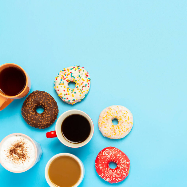 Tasty donuts and cups with hot drinks, coffee, cappuccino, tea on a blue background. Concept of sweets, bakery, pastries, coffee shop, meeting, friends, friendly team. square. Flat lay, top view. - Foto, imagen