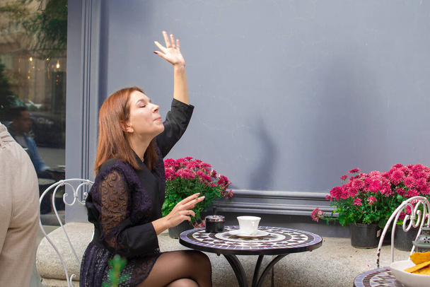 Ένα κορίτσι με ένα τσιγάρο κάθεται σε ένα καφέ και με μια χειρονομία του χεριού της καλεί το σερβιτόρο - Φωτογραφία, εικόνα