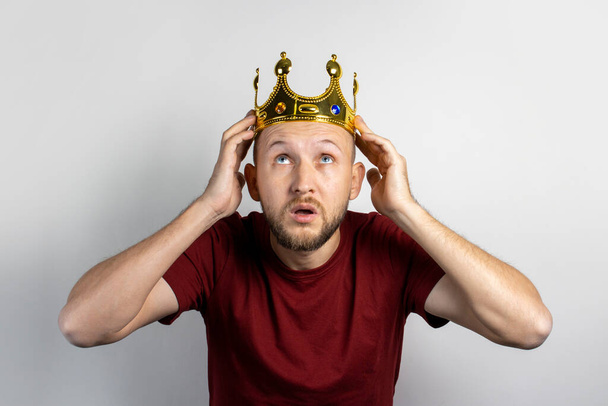 Young man tries on a golden crown on a light background. Concept is king, luck, gain, rich, dream, goal, aspiration. Banner. - Foto, Bild