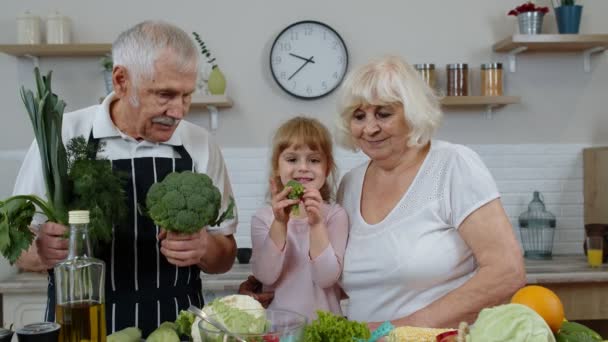 Nieta niña con abuelos mayores recomendando comer alimentos vegetales crudos. Dieta nutricional - Imágenes, Vídeo