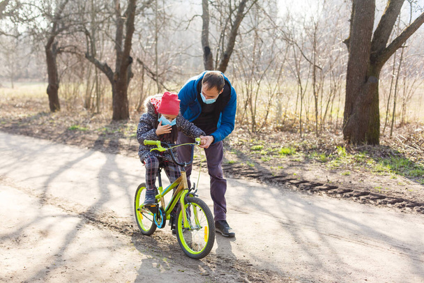 Кавказький батько допомагає дочці їздити на велосипеді з захисною маскою для захисту pm2.5 та синдрому Коронавірусу Ковід-19.. - Фото, зображення