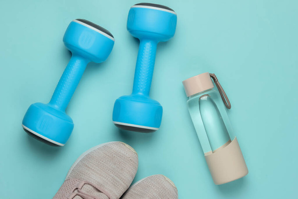 Flat lay style concept of healthy lifestyle, sport and fitness. Sports shoes for running, dumbbells, bottle of water on blue pastel background. Top view - Photo, Image