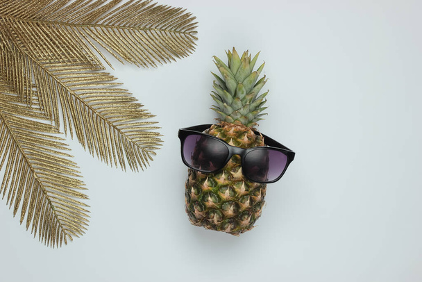 Güneş gözlüklü ananas ve beyaz arka planda altın palmiye yaprakları. Tropikal konsept. Üst görünüm - Fotoğraf, Görsel