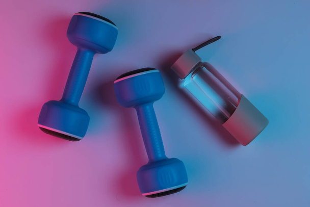 Fitness, sport koncepció. Gombócok és egy üveg víz. Neon rózsaszín kék éjszakai fény.  - Fotó, kép