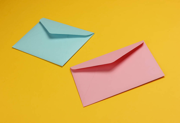 Two envelopes of pink and blue pastel colors on a yellow background. Mockup for valentines day, wedding or birthday - Fotografie, Obrázek