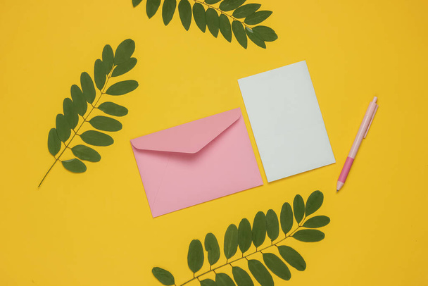 Zarfta yeşil yapraklı sarı arka planda bir mektup ve kalem var. Sevgililer günü, düğün ya da doğum günü. Üst görünüm - Fotoğraf, Görsel