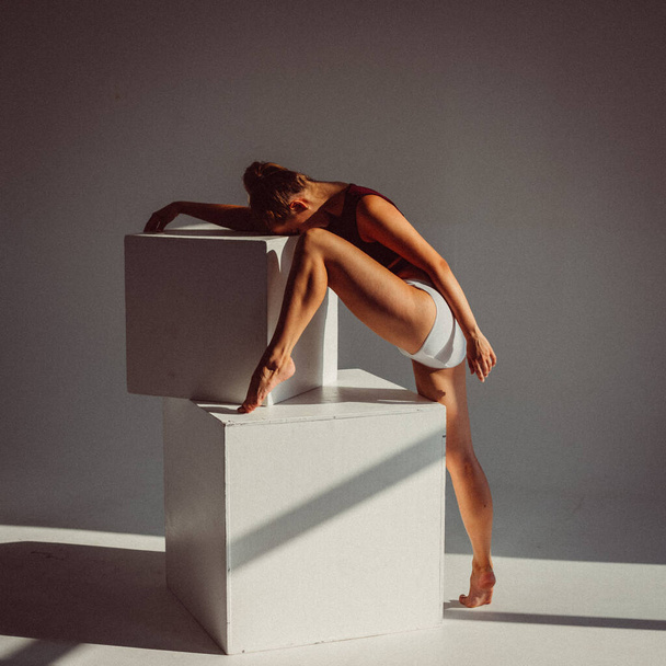A young girl, a gymnast, with a plastic figure, makes plastic eases on cubes in the studio, sunlight from the window shines on her. - Foto, Bild