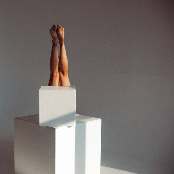 Una chica joven, con una figura de plástico, lame cubos blancos en el estudio, hace que el plástico se alivie, la luz del sol de la ventana brilla en ella. - Foto, Imagen