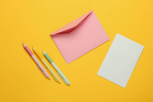 Envelop met een letter en pennen op gele achtergrond. Valentijnsdag, bruiloft of verjaardag. Bovenaanzicht - Foto, afbeelding