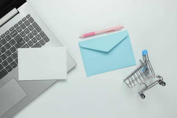 Laptop and envelope with letter, shopping trolley on white background. Valentine's day. Top view - Foto, Imagem