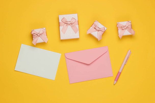 Envelop met brief en pen, dozen met geschenken op gele achtergrond. Kerstmis, Valentijnsdag, verjaardag. Bovenaanzicht - Foto, afbeelding