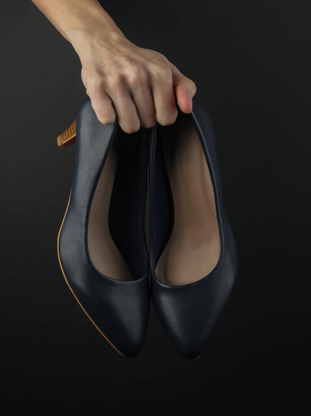 Mano femminile tiene scarpe tacco alto in pelle su sfondo nero - Foto, immagini