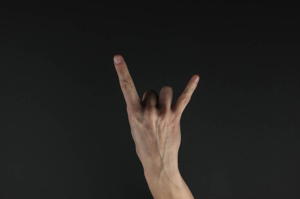 La mano femenina muestra un gesto de roca (cuernos) sobre un fondo negro - Foto, imagen