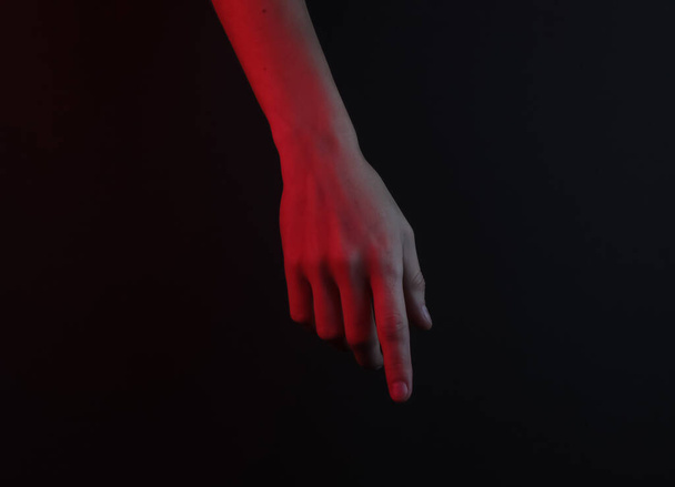 Female hand touches something on a black background. Red neon night light - Φωτογραφία, εικόνα