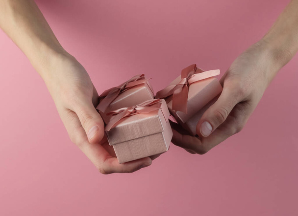 Female hands hold gift boxes on a pink pastel background. Concept of birthday, christmas, valentines day - Photo, Image