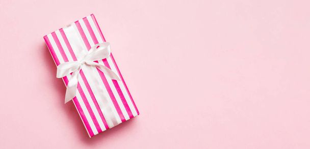 envuelto Navidad u otro regalo hecho a mano de vacaciones en papel con cinta blanca sobre fondo rosa. Caja de regalo, decoración de regalo en mesa de colores, vista superior con espacio para copiar. - Foto, Imagen