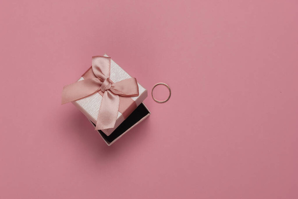 Gift box with bow and gold ring on pink pastel background. Wedding concept. Jewelry. Top view. Flat lay - Photo, Image