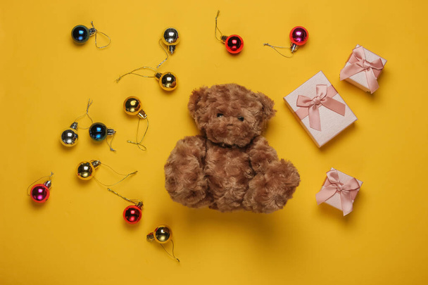 Teddy maci, ajándékdobozok, karácsonyi játékok sárga háttérrel. Karácsonyi koncepció. Felülnézet - Fotó, kép
