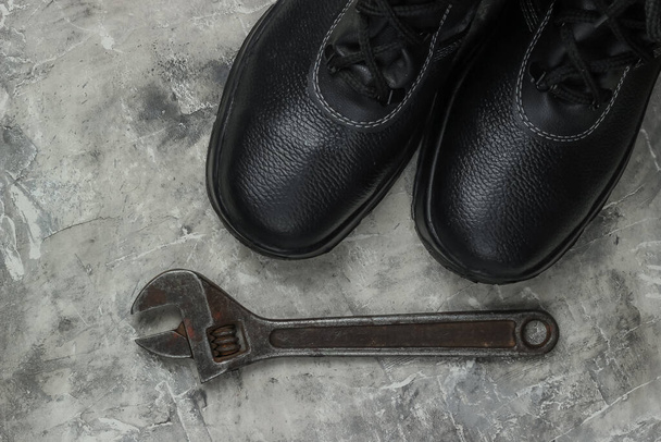 Work leather shoes and wrench. Industrial working tools and instruments, safety equipmen on gray concrete background. Top view - Photo, Image