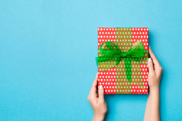 Woman arms holding gift box with colored ribbon on blue table background, top view and copy space for you design. - 写真・画像