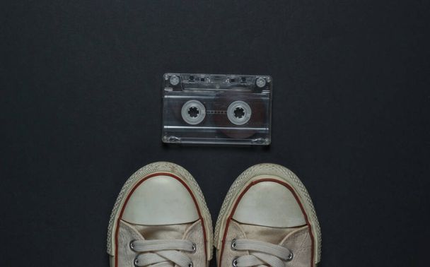 Ретро старые кроссовки и аудиокассеты на черном фоне. 80-е. Вид сверху - Фото, изображение