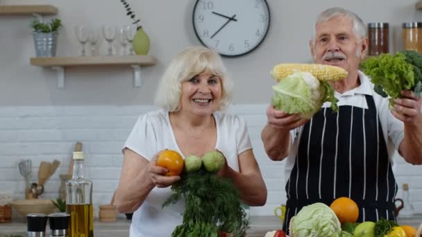 Starší muž a žena doporučují jíst syrové zeleninové jídlo. Starší prarodiče pár v kuchyni - Záběry, video
