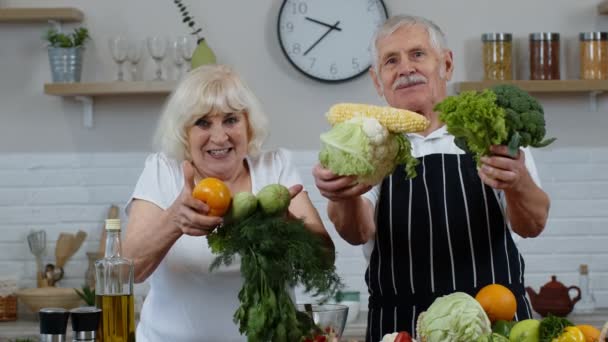 Abuelos mayores pareja en la cocina. Hombre y mujer maduros recomiendan comer alimentos vegetales crudos - Imágenes, Vídeo