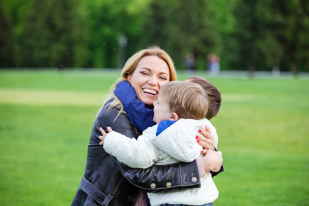 Happy young woman hugging two sons and laughing in park - Photo, Image