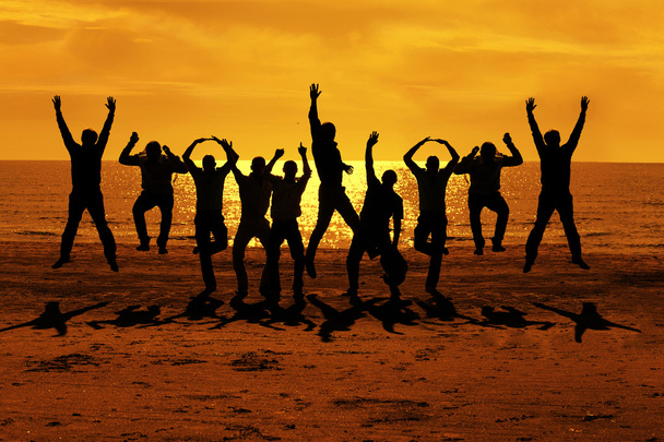 Gli amici maschi si divertono in estate e saltano sul tramonto vicino al mare mettendo le mani fino al cielo arancione
 - Foto, immagini
