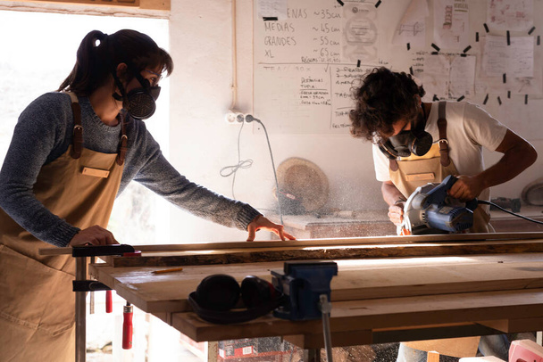 Jovem casal de carpinteiro trabalhando e artesanato com madeira em uma oficina de construção de móveis para design de interiores. Jovens empresários casal executando uma pequena empresa em uma carpintaria. Empresários. - Foto, Imagem